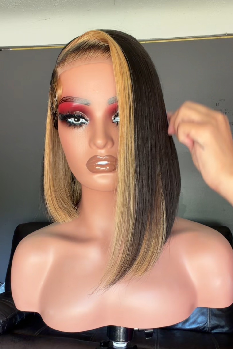 Mannequin head with a blonde wig on a tripod in a room.